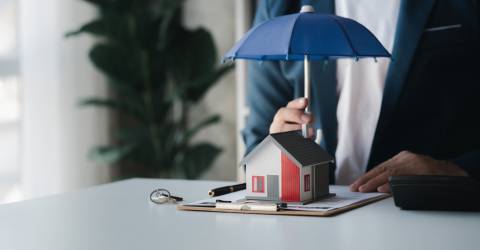 Man achter een bureau houdt een paraplu boven een woning waaronder een formulier ligt