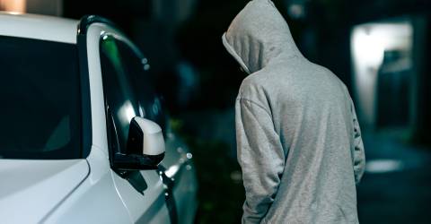 auto-inbraken; man loopt in het donker langs een witte auto en kijkt naar binnen 